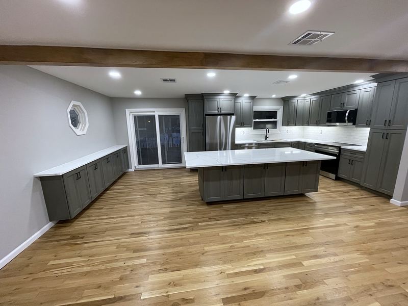 Open kitchen with gray shaker cabinets, white quartz island and wide-plank oak floors